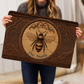 Person holding an ornate bee doormat with woodgrain styling, floral details, and framed artwork