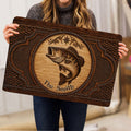 Person holding a rustic fishing doormat featuring a central fish illustration and ornate brown border