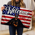 Person holding a patriotic Doberman doormat featuring flag colors and welcome artwork