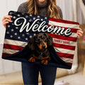 Person holding a patriotic dachshund welcome doormat with stars, stripes and family-themed artwork