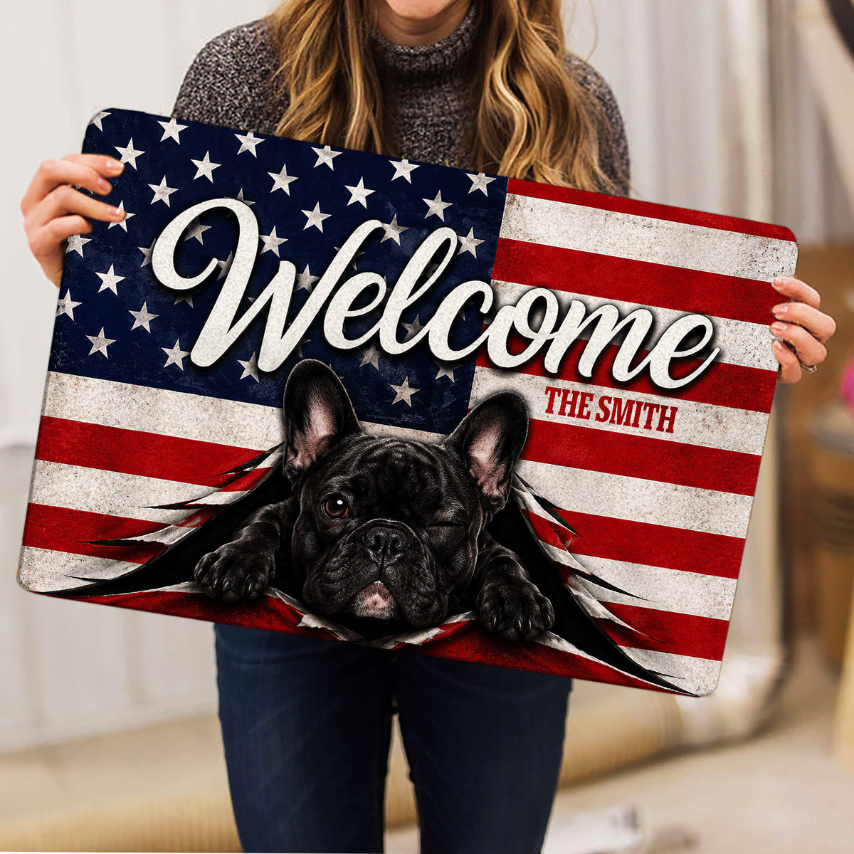 Person holding a French Bulldog doormat featuring a bold American flag welcome design