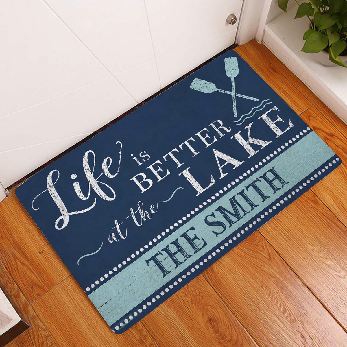 Lake house doormat displayed by a white door on a warm wood floor with crossed oar artwork