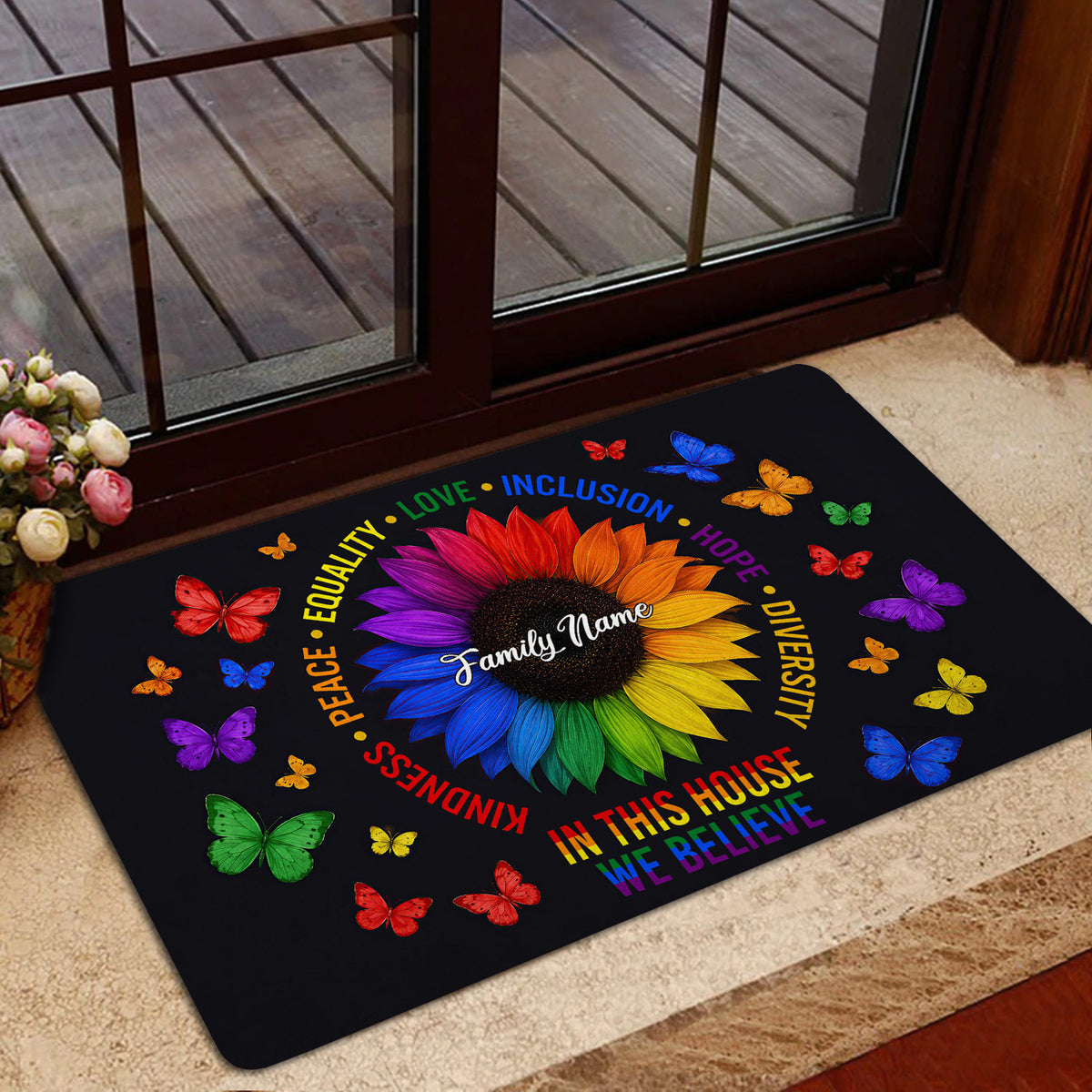 Rainbow LGBT doormat with sunflower and butterfly artwork placed inside a glass doorway near a deck