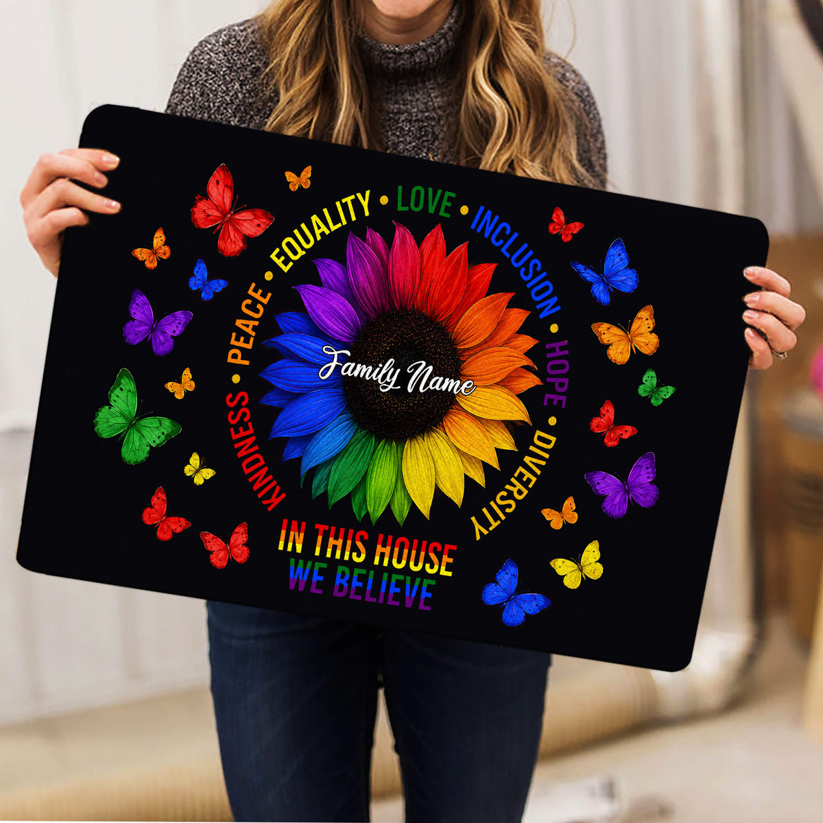 Person holding an LGBT doormat featuring a rainbow sunflower, butterflies, and messages of equality and inclusion