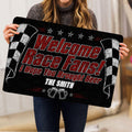 Person holding a black racing doormat featuring bold red lettering, checkered flags, and beer mugs