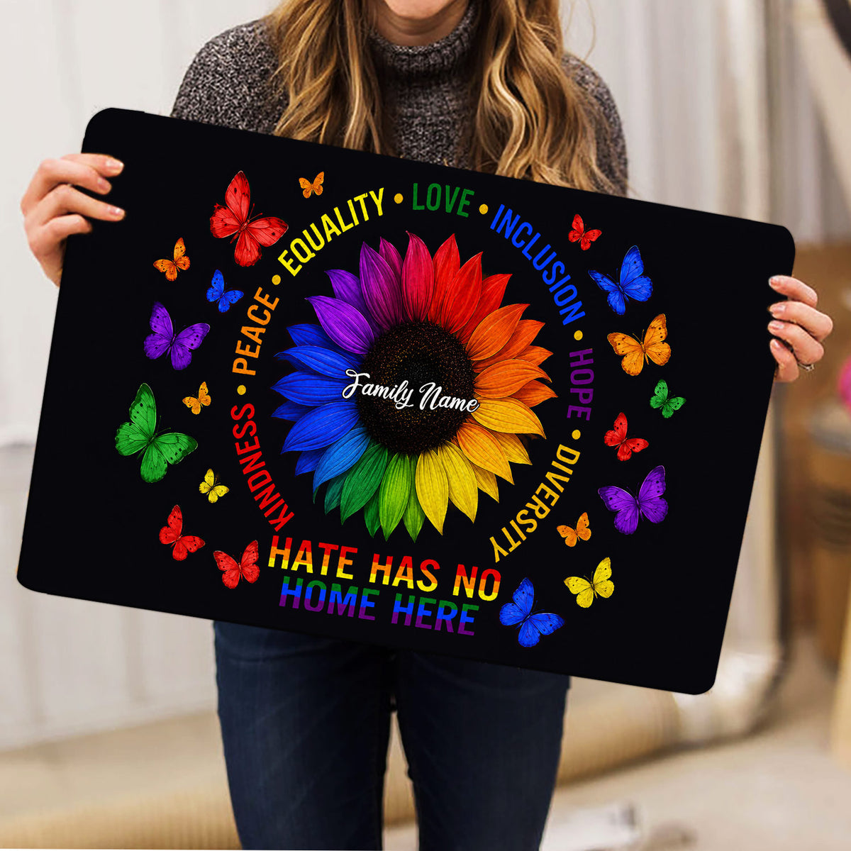 Person holding an LGBT pride doormat featuring a vibrant sunflower, butterflies, and a message of acceptance
