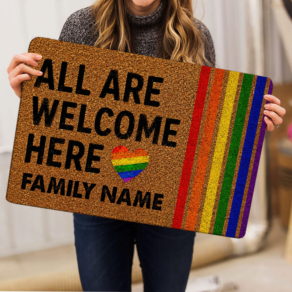 Person holding a colorful LGBT pride doormat with rainbow heart and inclusive welcome design