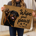 Person holding a Rottweiler doormat featuring a raised paw, paw prints, and tan artwork