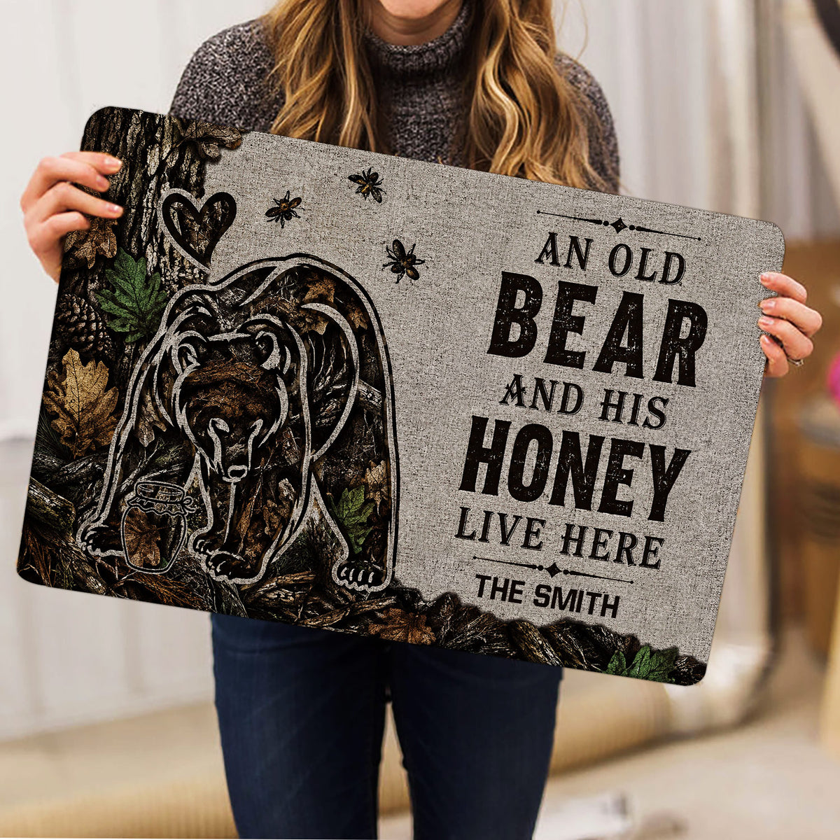 Bear doormat held indoors, showing the detailed forest scene, bees, honey jar, and decorative lettering