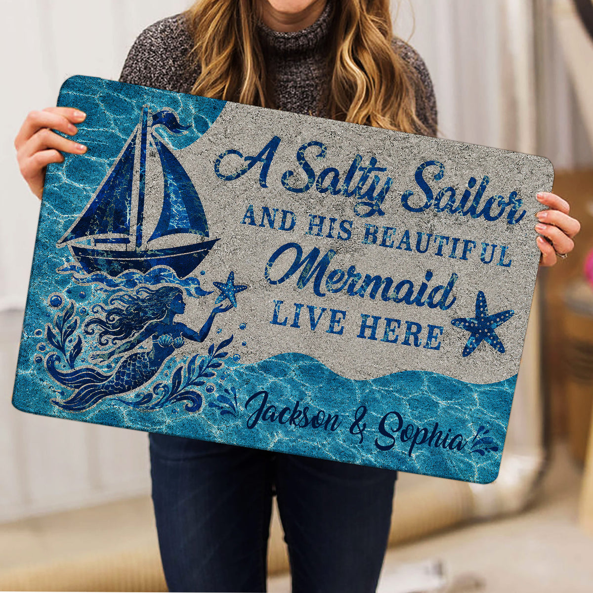 Mermaid doormat held indoors, displaying a blue ocean scene with sailboat and starfish