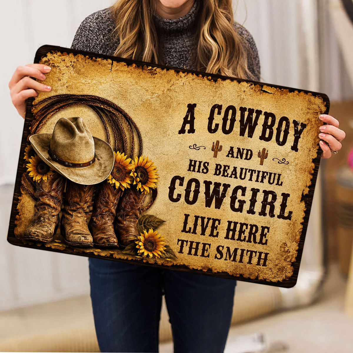 Person holding a western cowboy doormat featuring a hat, boots, sunflowers, and bold rustic lettering
