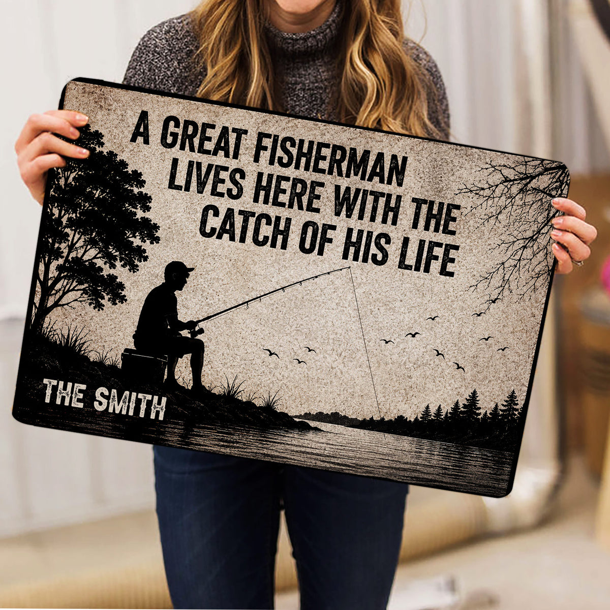 Fishing doormat held indoors, showing a silhouetted fisherman casting across a lake with trees and birds