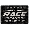 Black racing doormat with bold white welcome lettering, stars, checkered accents, and tire-track graphics