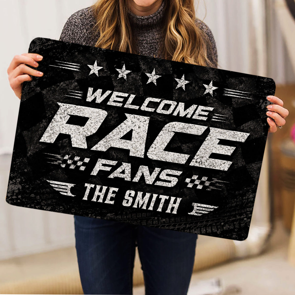 Racing doormat held indoors showing bold white lettering, star accents, checkered flags, and tire-track texture