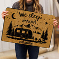 Person holding a camping doormat featuring a camper, mountains, pine trees, campfire, moon, and stars
