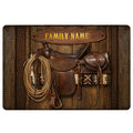 Cowboy doormat featuring a western saddle, coiled lasso, rustic wood texture and warm brown tones