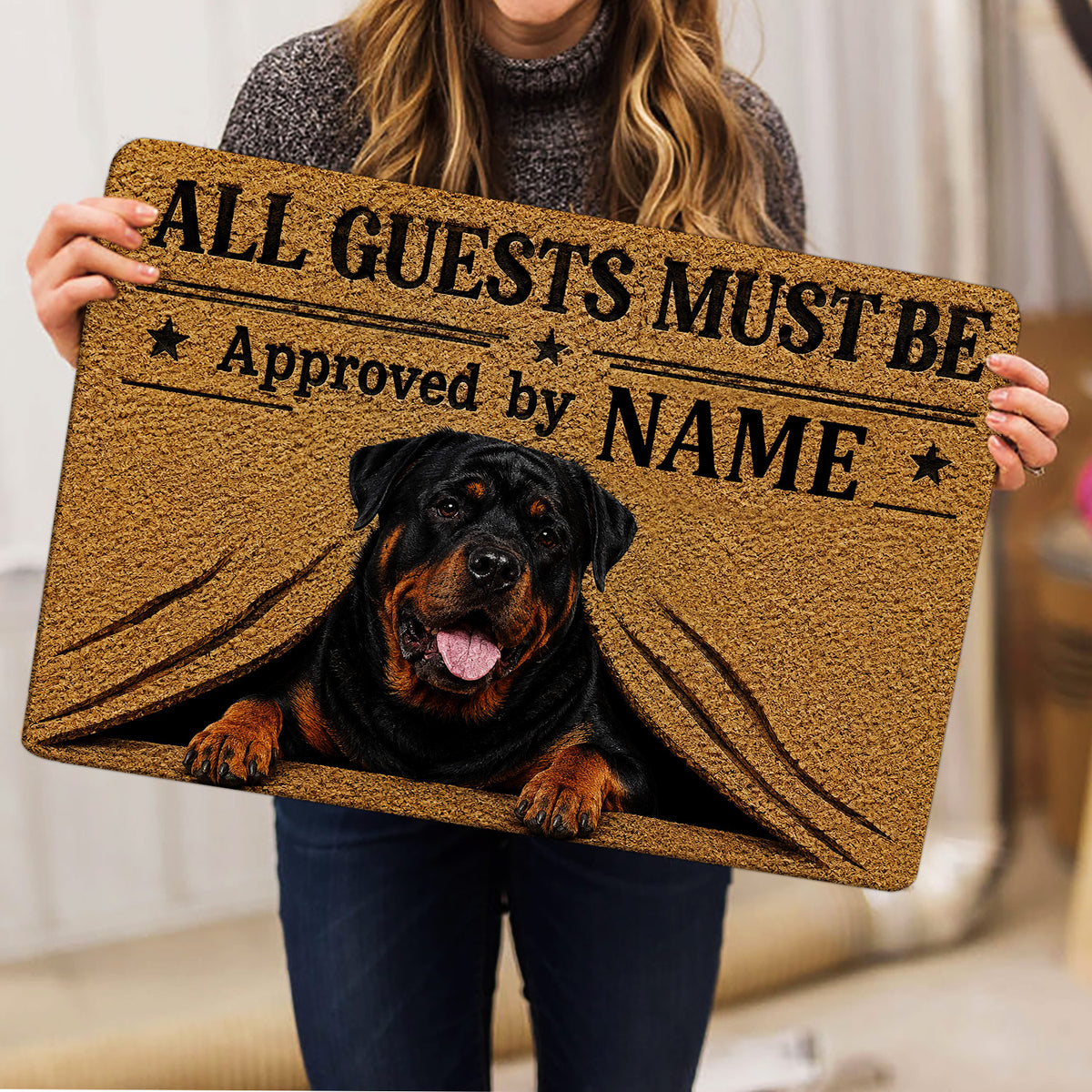 Person holding a Rottweiler doormat featuring a tan background, black typography, stars, and dog artwork