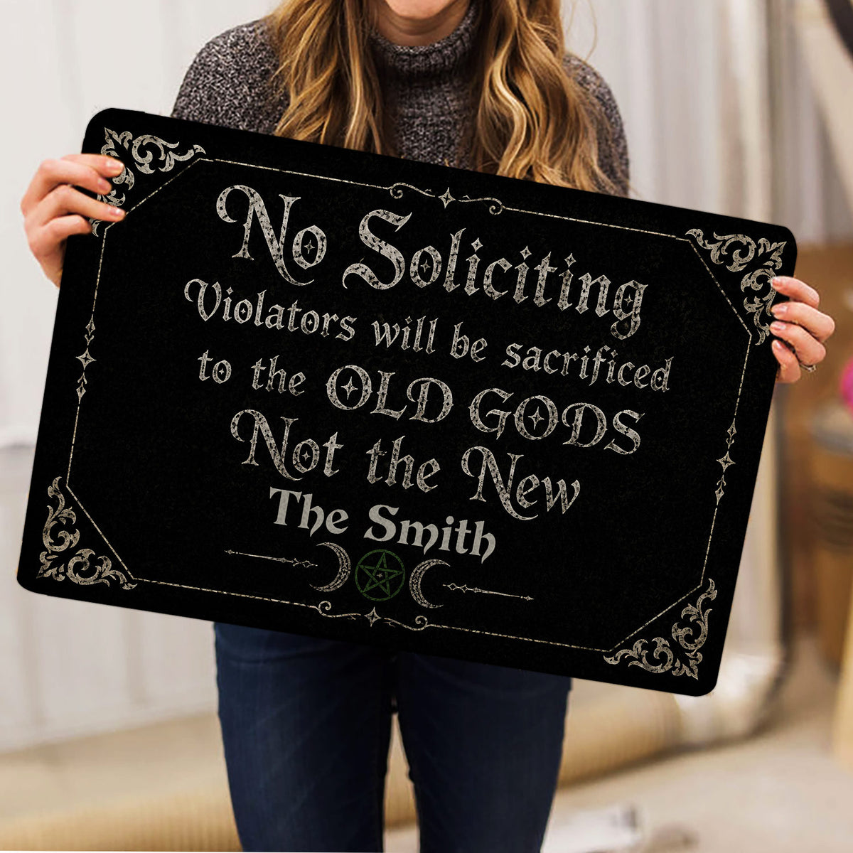 Person holding a black Wicca doormat featuring gothic lettering, crescent moons, and a pentagram