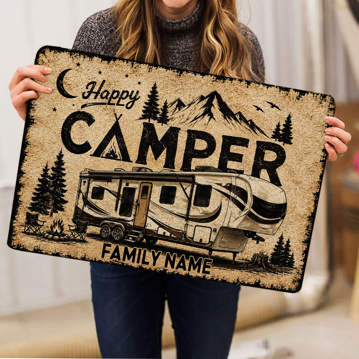 Camping-themed doormat held indoors, showing an RV, mountains, trees and campfire scene