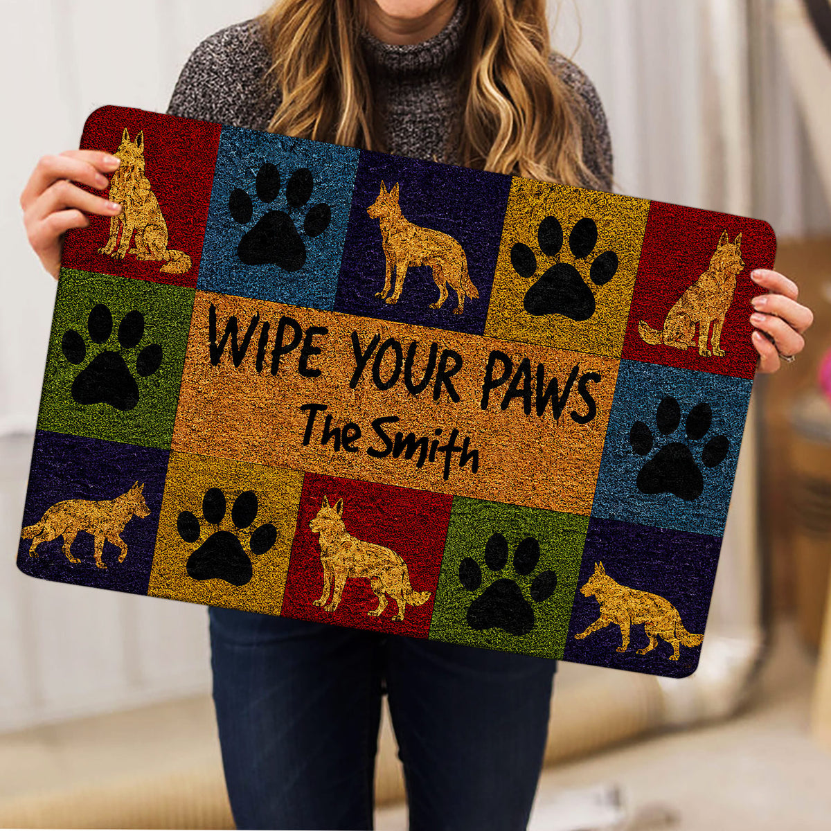 Person holding a colorful German Shepherd doormat featuring paws and dog illustrations
