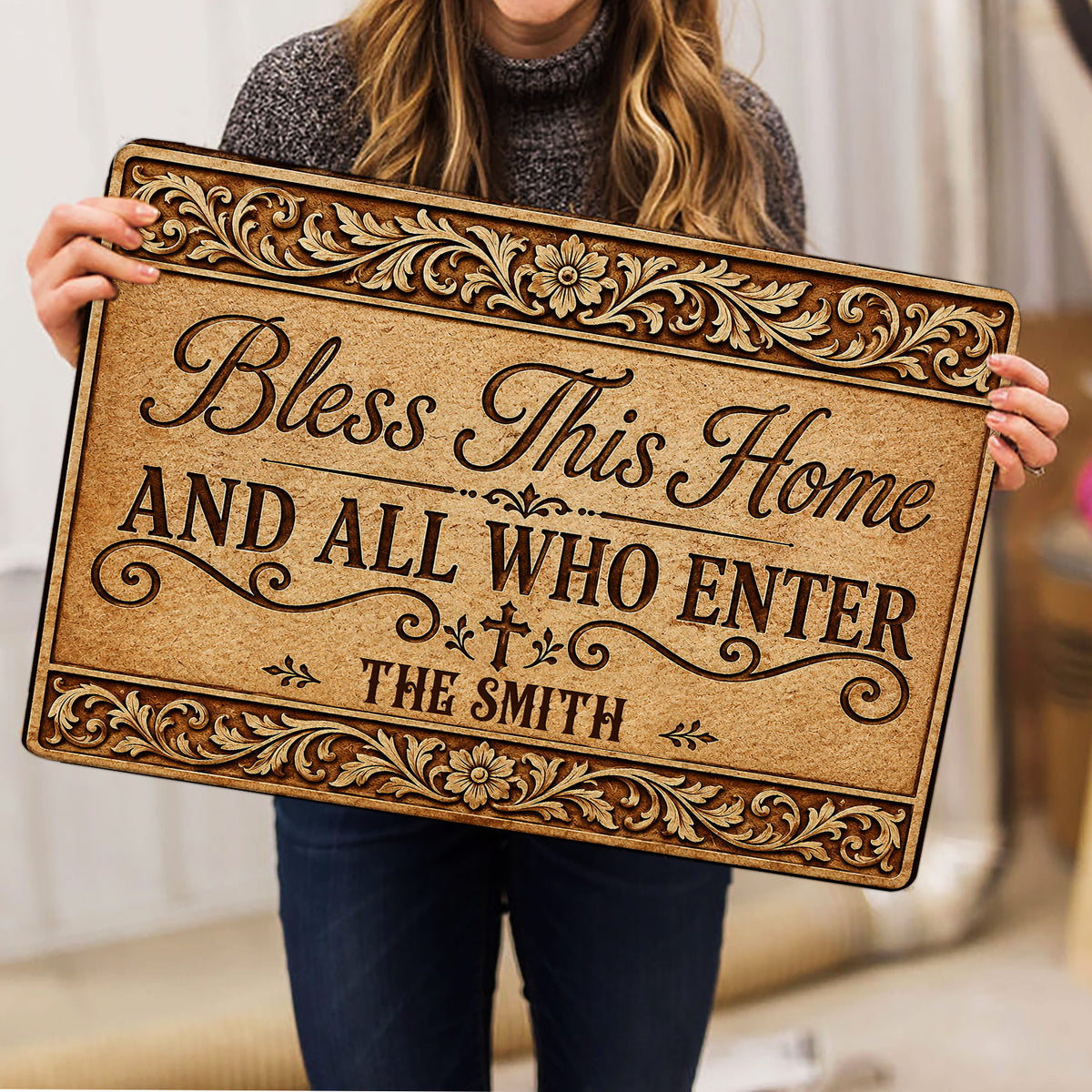 Person holding an ornate Christian blessing doormat with floral scrollwork and a cross