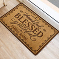 Christian front door mat on light wood flooring featuring blessed and grateful wording with decorative flourishes