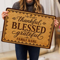 Person holding a Christian doormat featuring a cross, grateful and blessed wording, and an ornate brown border