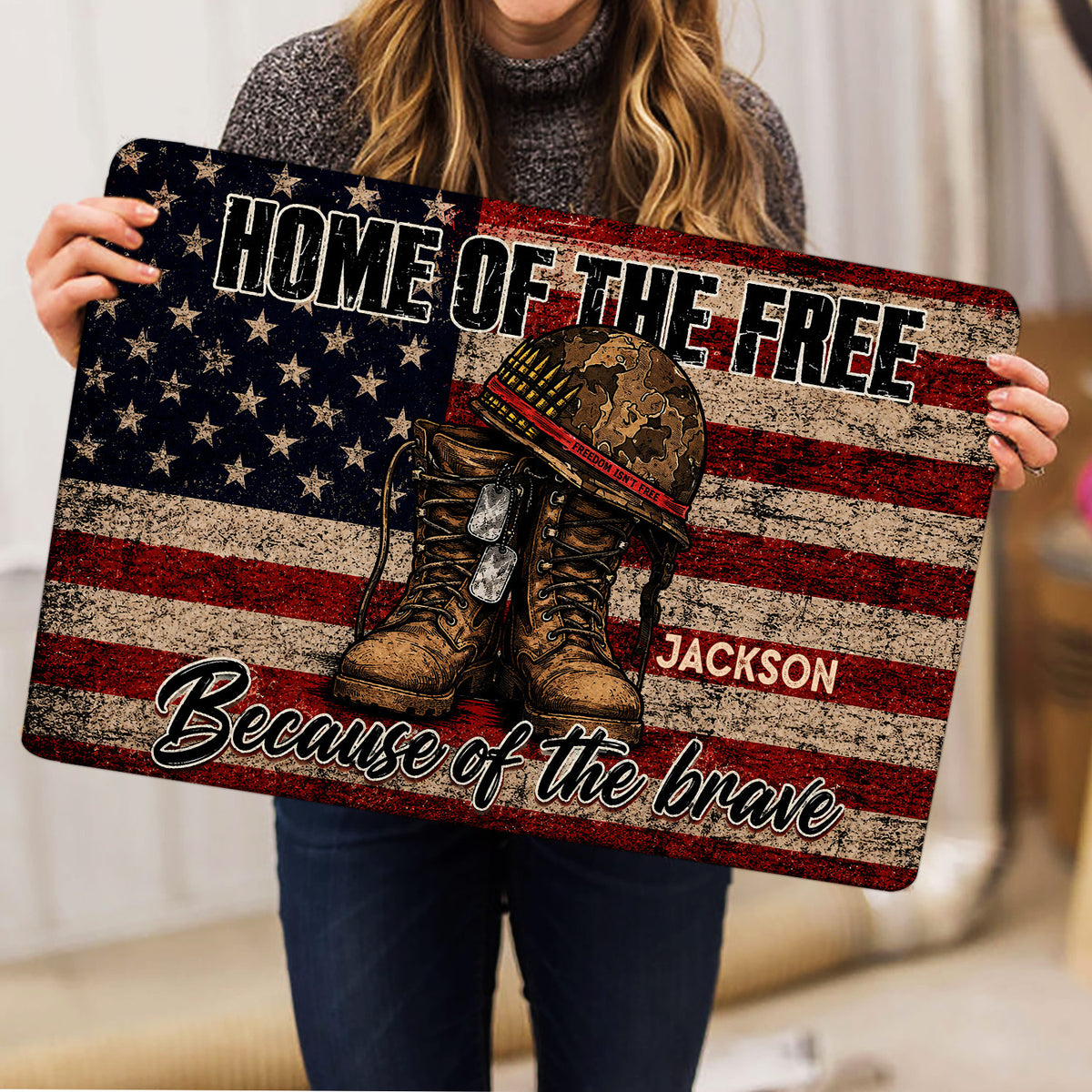 Person holding a patriotic veteran doormat featuring military boots, helmet, dog tags, and flag design