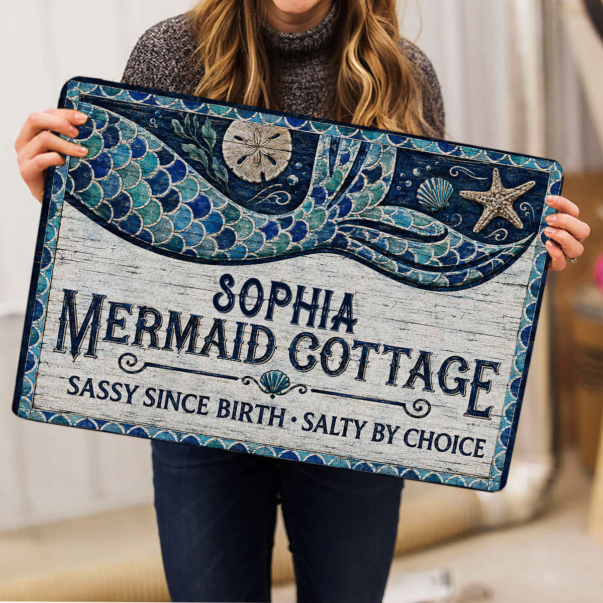 Mermaid doormat held indoors, showing detailed blue tail scales, seashells, starfish, and rustic coastal styling