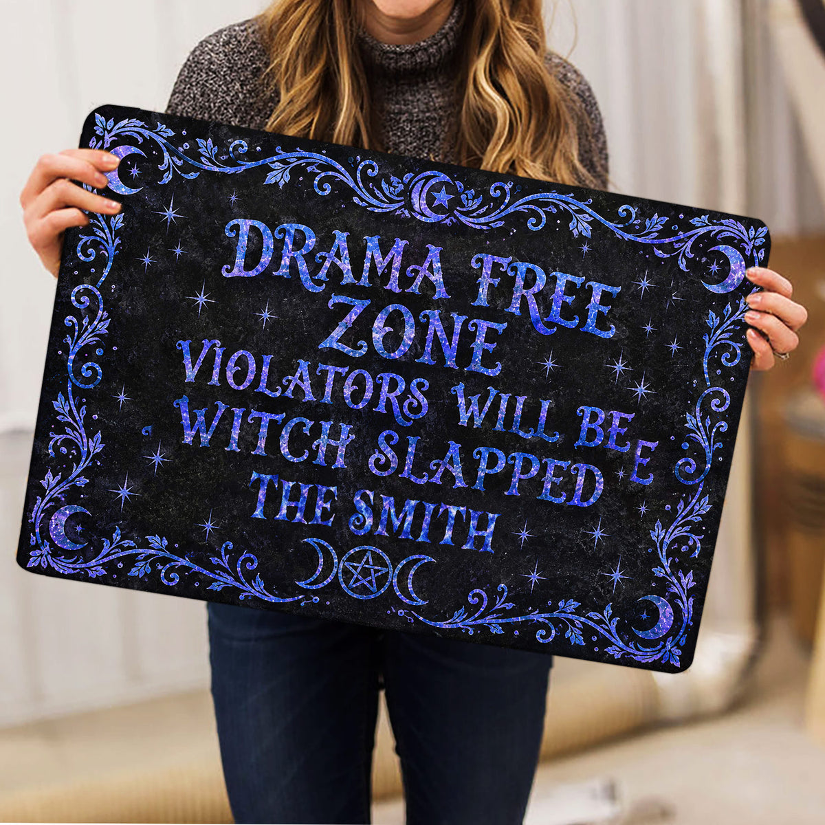 Person holding a black Wicca doormat featuring blue celestial symbols and ornate witchy artwork