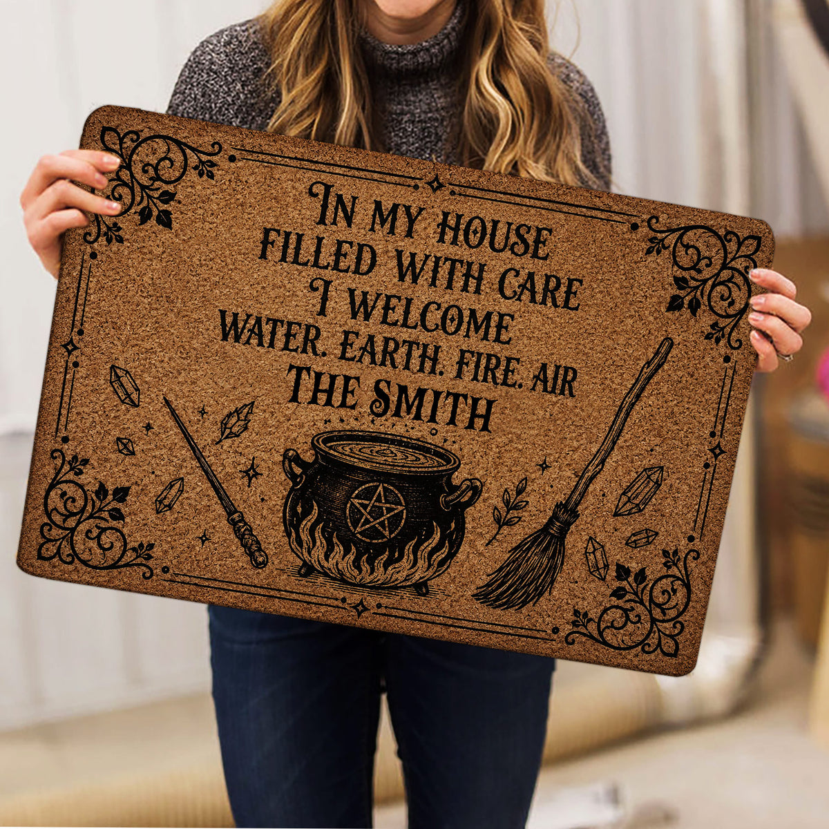 Person holding a Wicca doormat with cauldron, pentagram, broom, wand and crystal illustrations