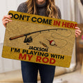 Fishing-themed doormat held indoors, showing the rod, reel, bobber and lure artwork