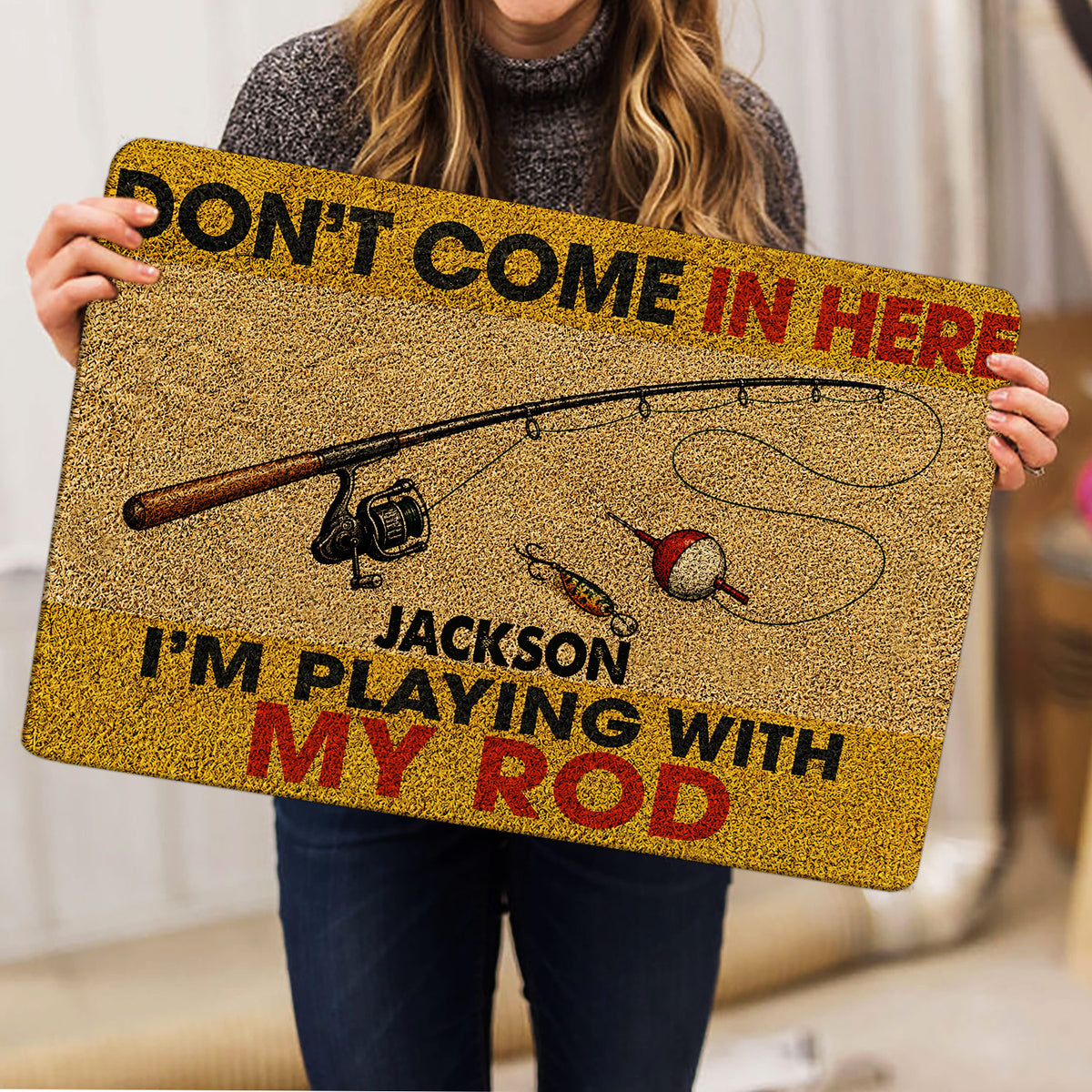 Fishing-themed doormat held indoors, showing the rod, reel, bobber and lure artwork