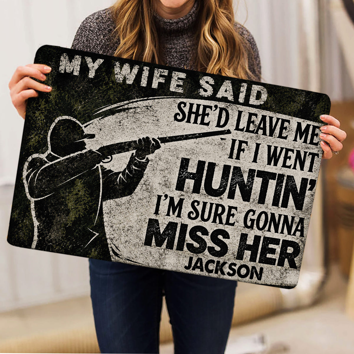 Person holding a hunter-themed doormat featuring a distressed black, gray, and green design