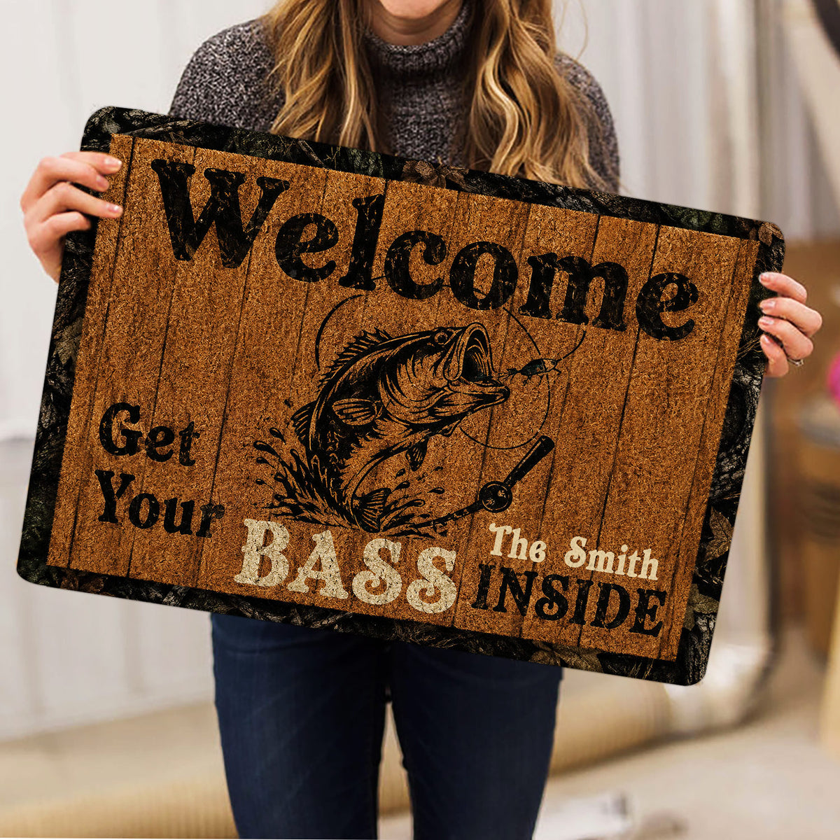 Person holding a rustic fishing doormat featuring a leaping fish and welcoming entryway artwork