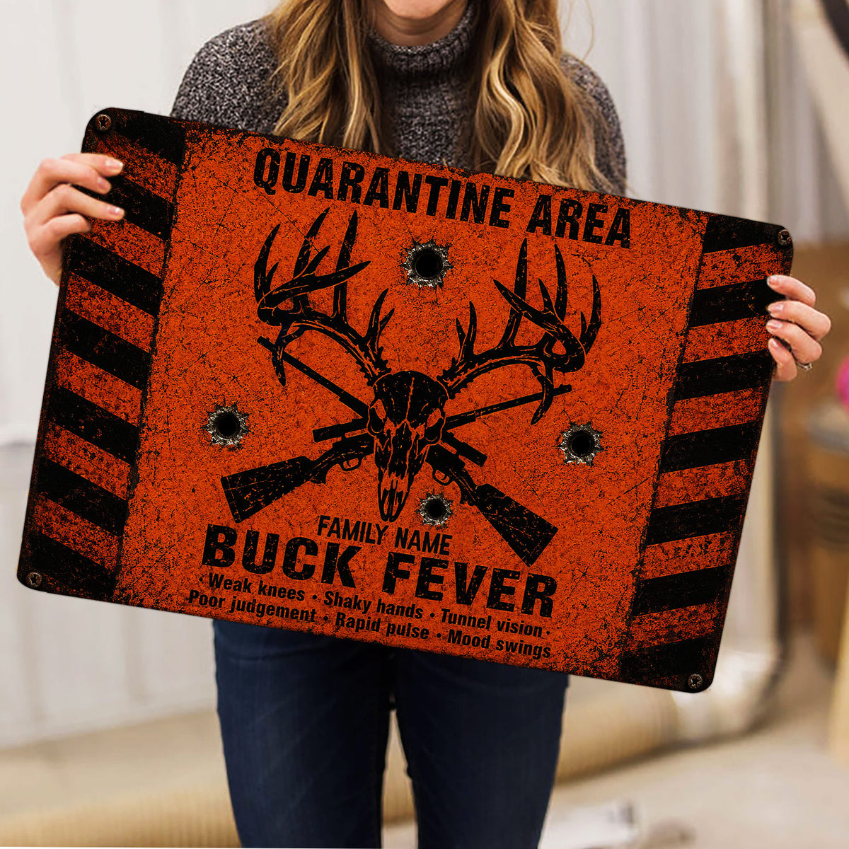 Person holding an orange and black hunting doormat featuring antlers, a buck skull and rifles