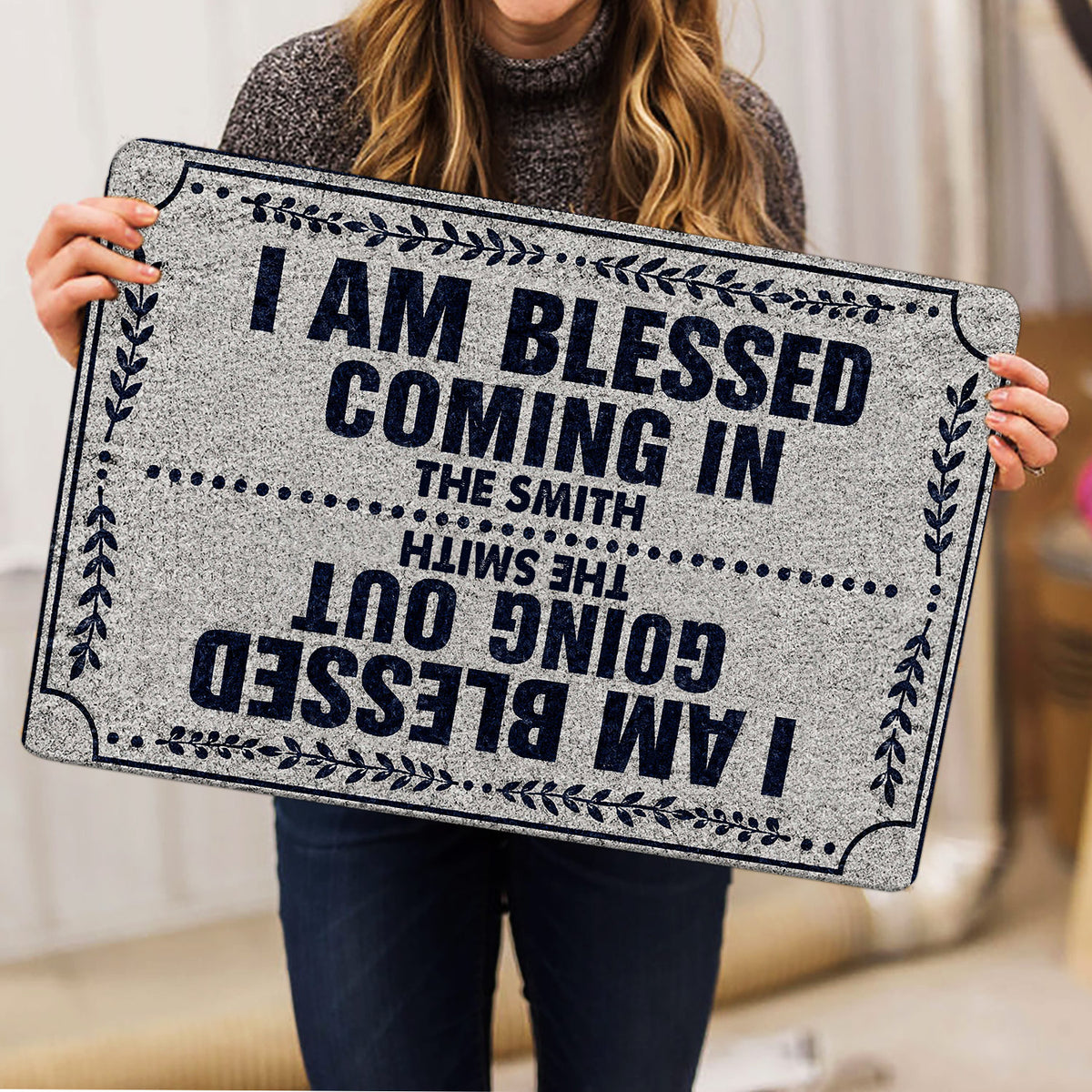 Person holding a Christian doormat featuring a bold welcoming message and navy botanical border