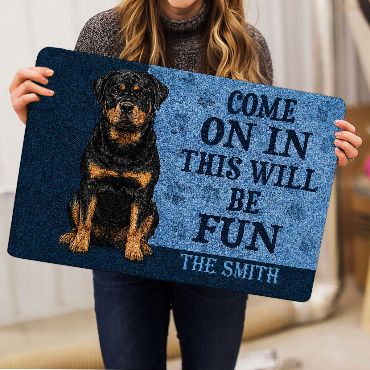 Rottweiler doormat held indoors, showing the full black and tan dog design and welcoming entryway artwork