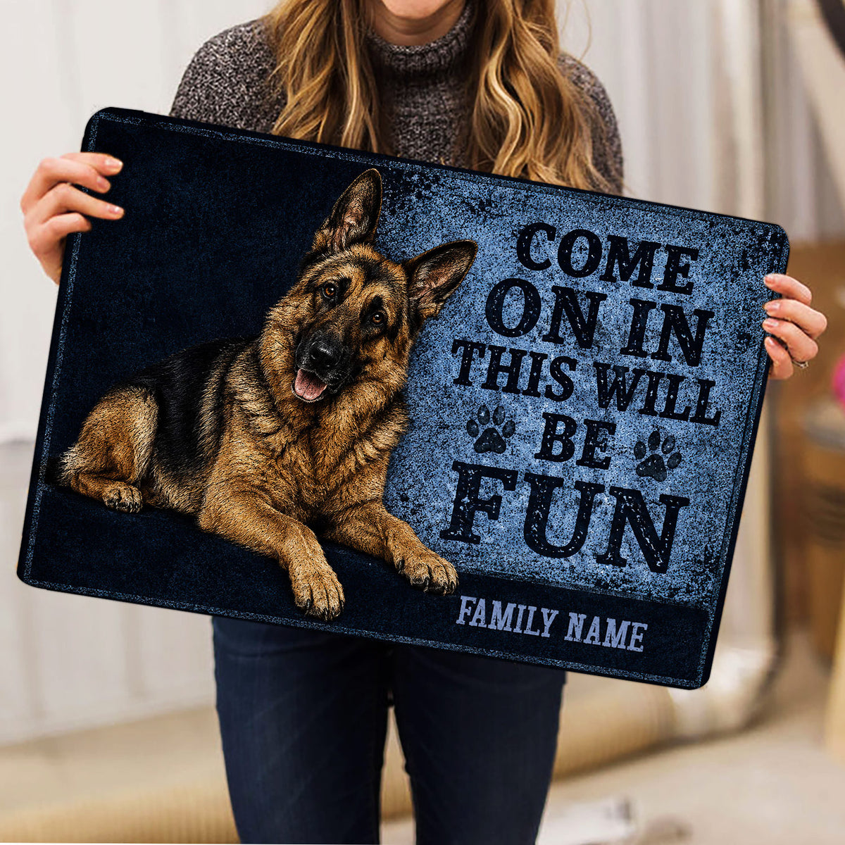 Person holding a German Shepherd doormat featuring blue artwork, paw prints, and welcome lettering