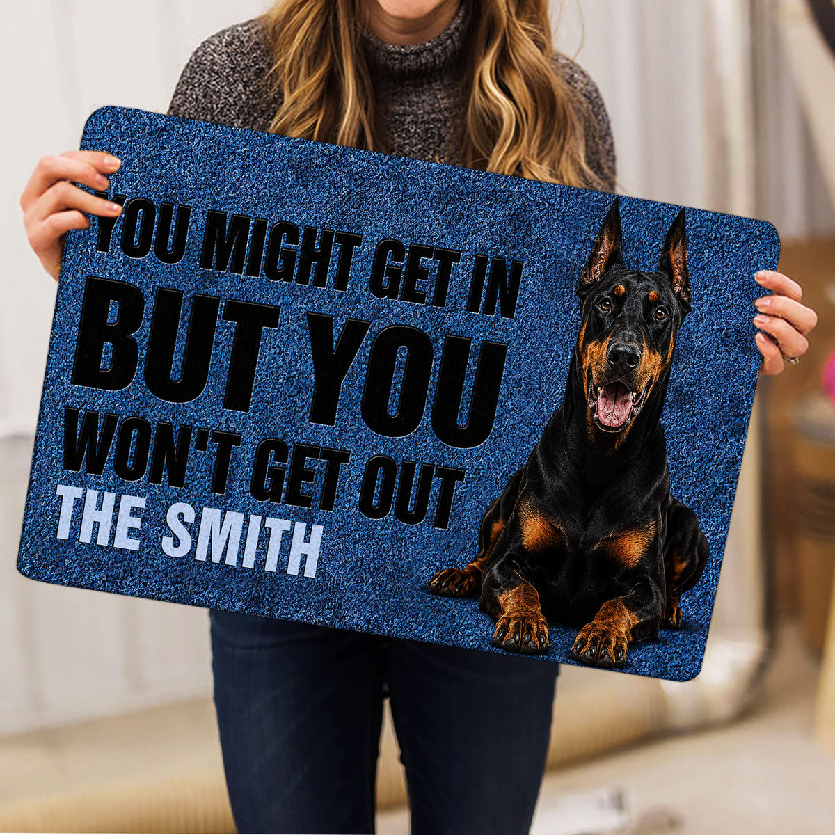Person holding a blue Doberman doormat featuring a bold warning design and seated dog artwork