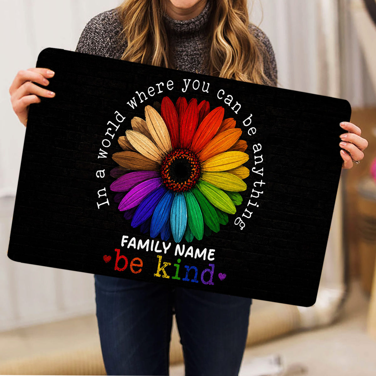 Person holding a black LGBT doormat featuring a vibrant rainbow flower design