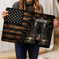 Person holding a veteran doormat featuring a distressed American flag, military boots, dog tags, and dark woodgrain design