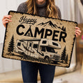 Person holding a camping doormat with an RV, mountains, pine trees, and family welcome artwork