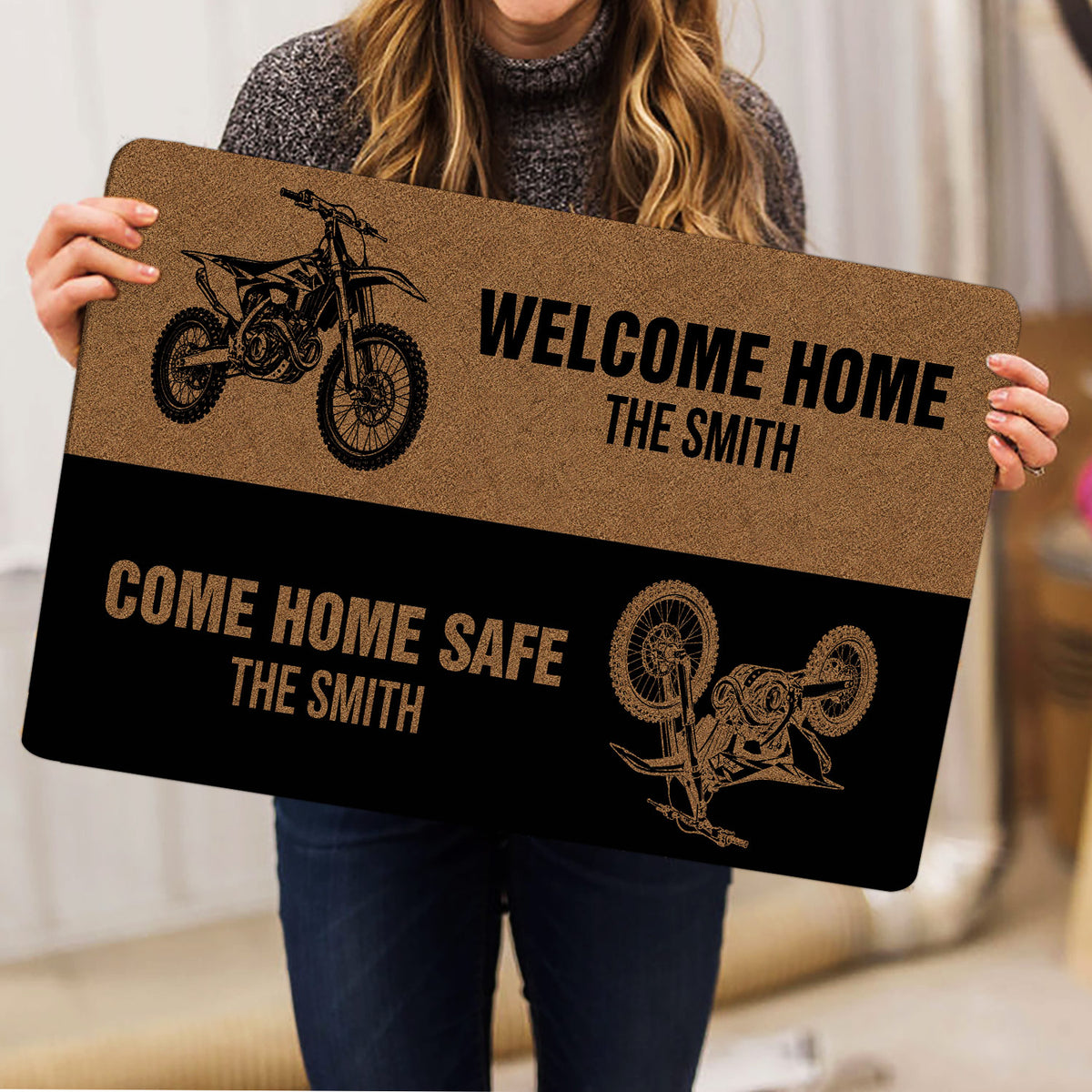 Person holding a motocross doormat with dirt bike artwork and bold welcome home messaging