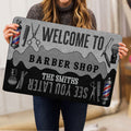 Person holding a barber shop doormat featuring barber poles, scissors, combs and welcome artwork