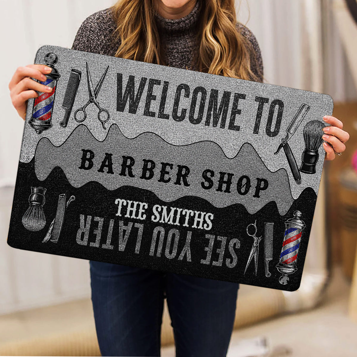 Person holding a barber shop doormat featuring barber poles, scissors, combs and welcome artwork