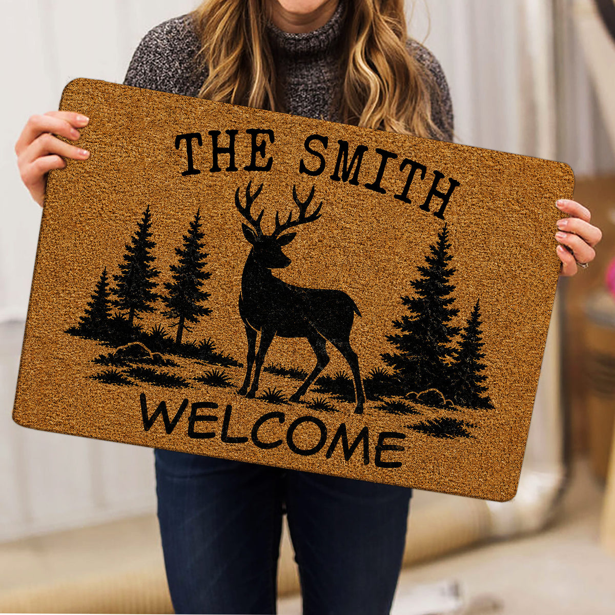 Person holding a tan deer hunting doormat featuring pine trees and welcome artwork