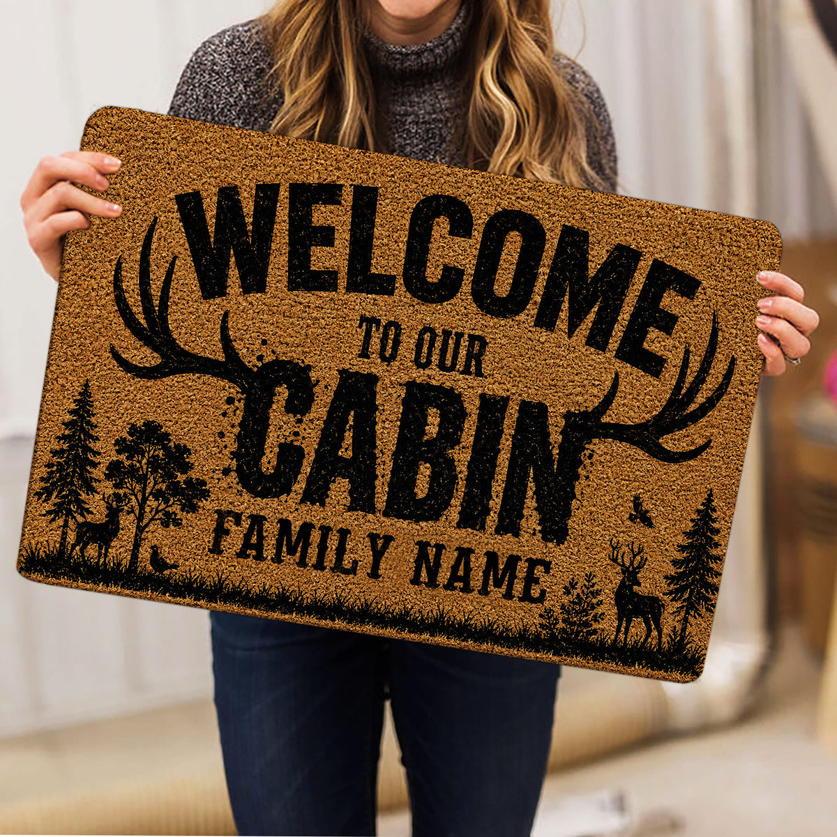 Person holding a hunting doormat featuring deer, antlers, trees, and rustic artwork