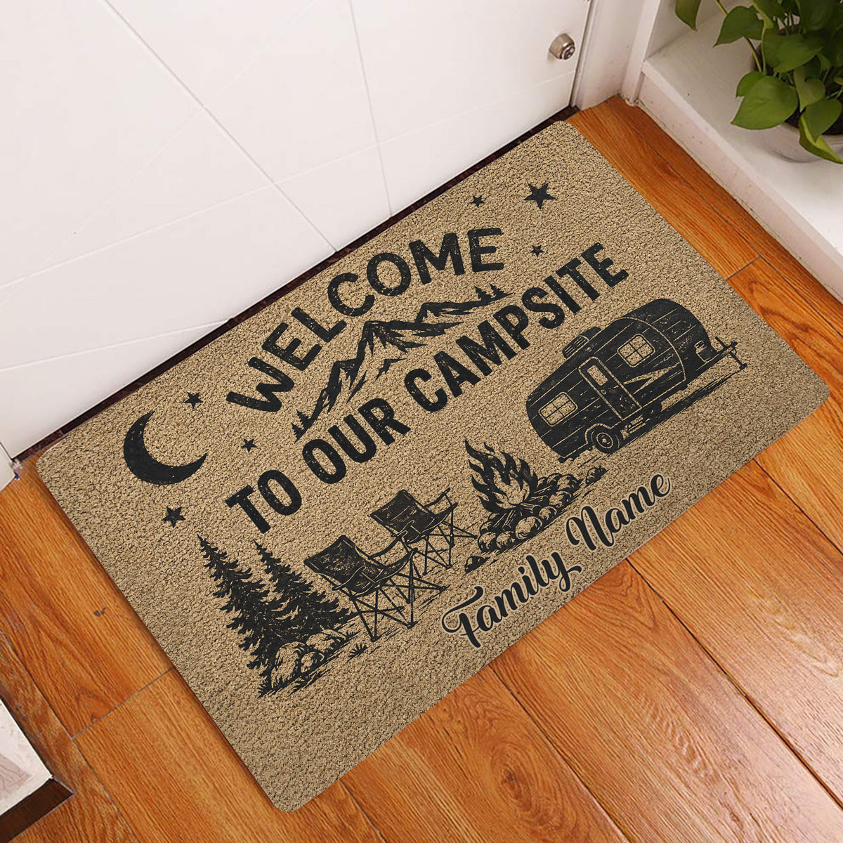Camping entryway doormat displayed beside a door on wood flooring with a mountain and travel trailer design