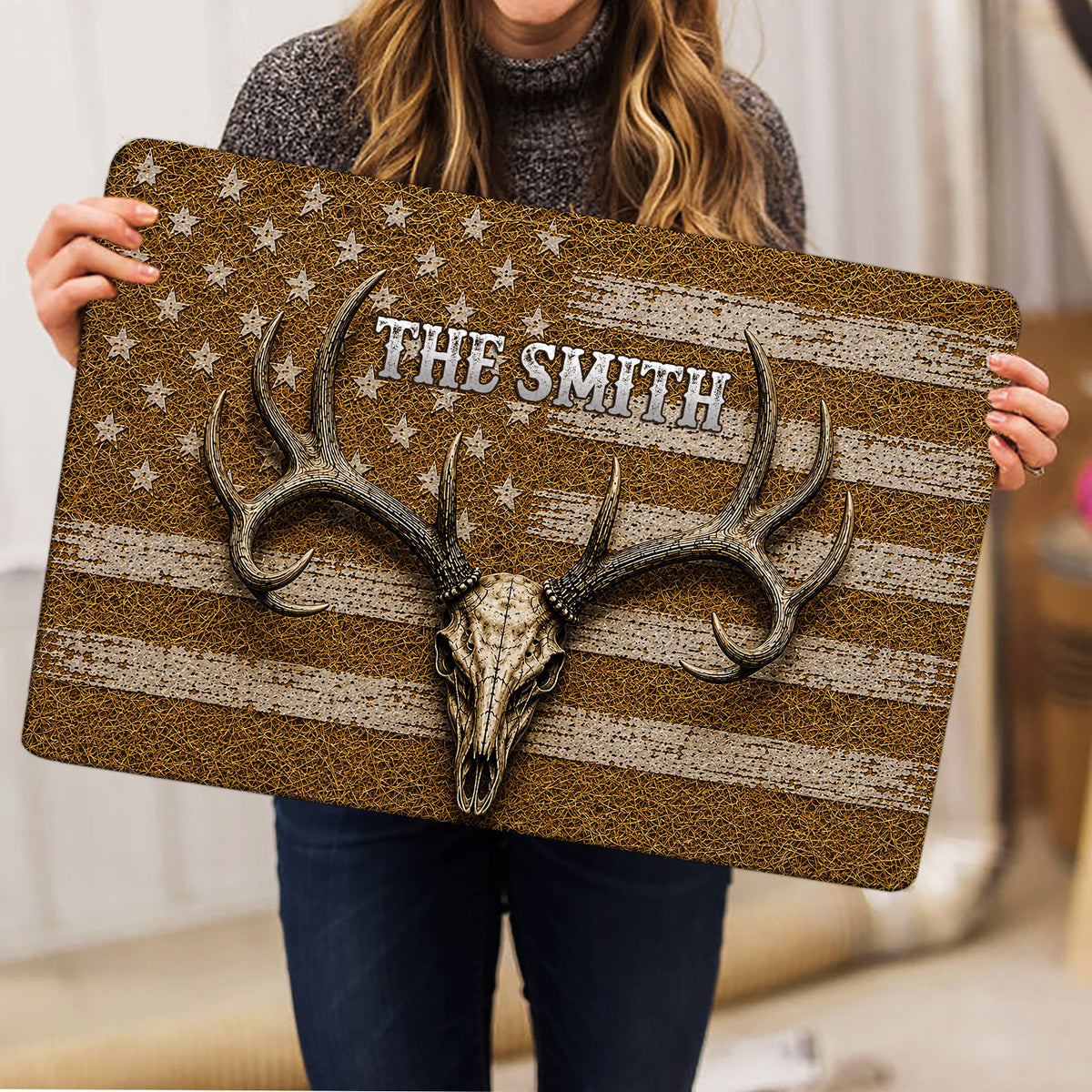 Person holding a hunting doormat featuring a deer skull, oversized antlers, stars and distressed stripes